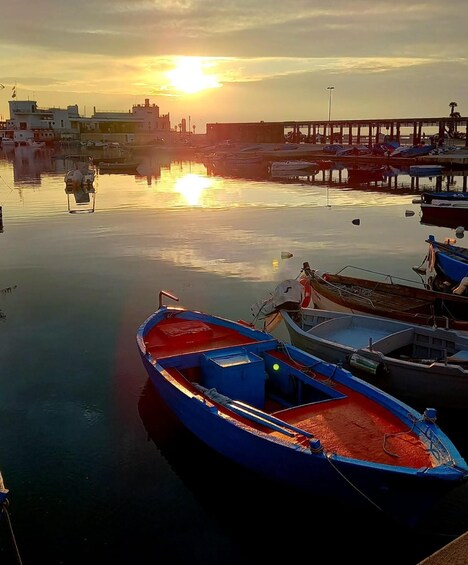 A harbor at sunset with boats docked, a pier, and buildings in the background. 4