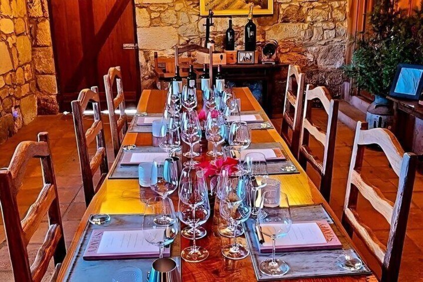 A long wooden dining table set with wine glasses, plates, and cutlery, surrounded by wooden chairs. 4