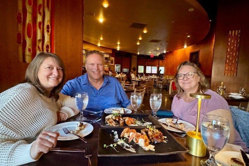 Three people dining at a restaurant with a variety of dishes on the table. 4