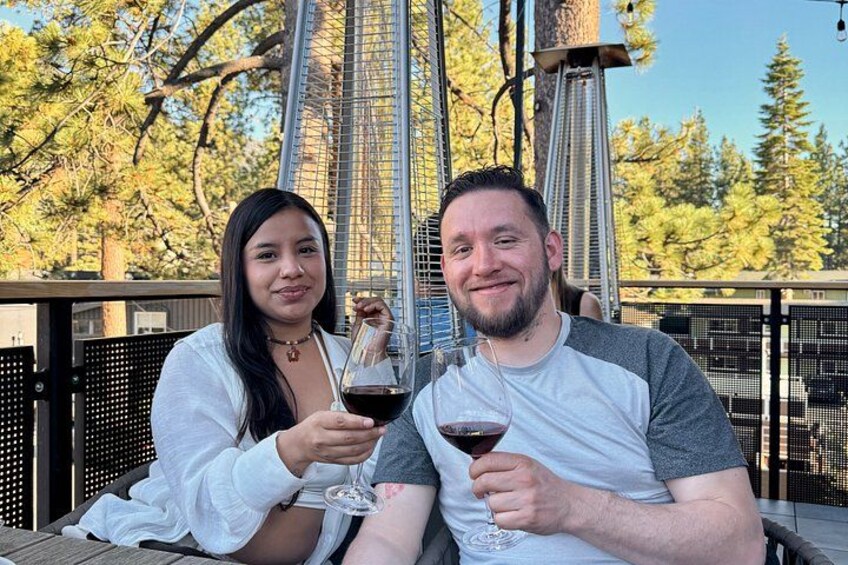Two people sitting at a table outdoors, holding wine glasses. 1