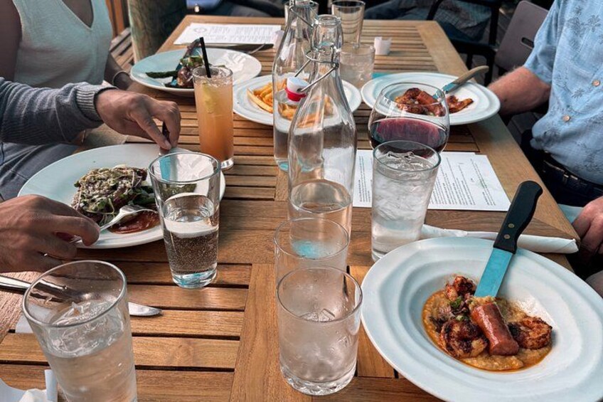 A wooden table with plates of food, glasses of water and drinks, and a bottle. 4