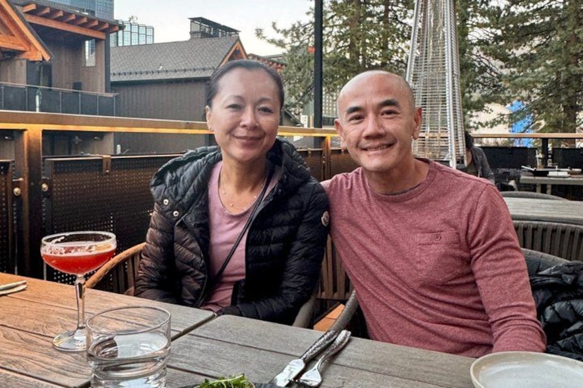 Two people sitting at an outdoor table with a drink and cutlery. 2