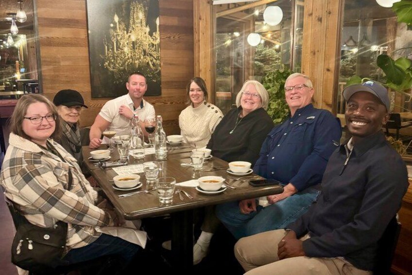 A group of people seated around a wooden table with plates, glasses, and cutlery. 3