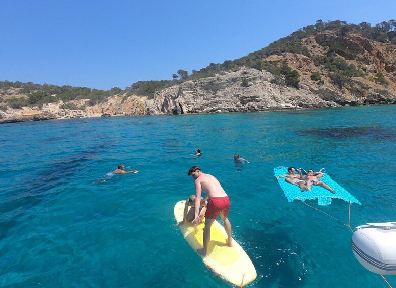 People swimming and surfing in a clear blue sea with rocky hills in the background. 5