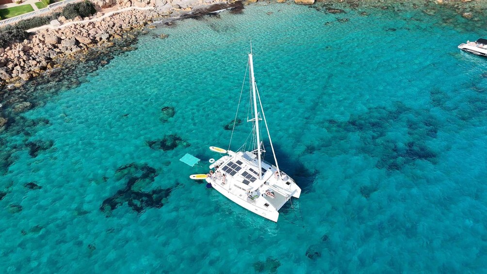 A sailboat anchored in clear turquoise waters with rocky shorelines. 4