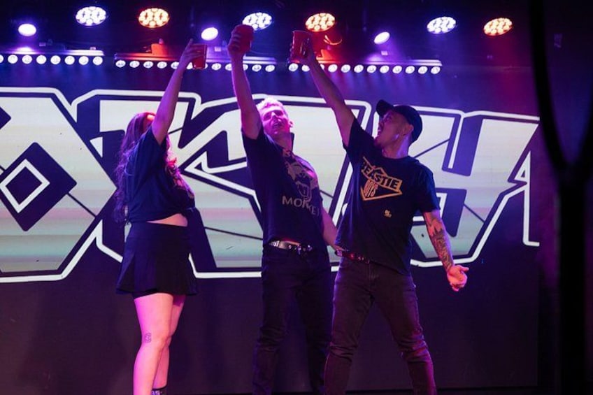 Three people on a stage with a large illuminated sign in the background. 3