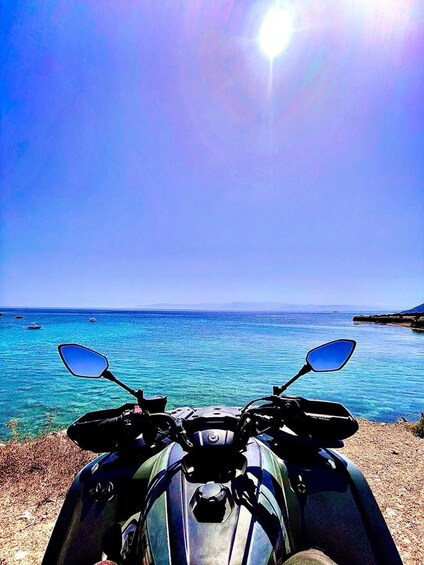 A motorcycle parked by the seaside with clear blue waters and boats in the distance. 1