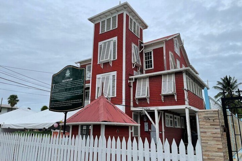 A red building with a white picket fence, a red umbrella, and a historical marker. 4