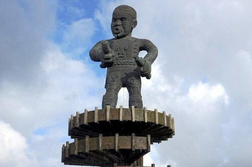 A large stone statue of a figure with outstretched arms, standing on a circular base with a cloudy sky in the background. 2