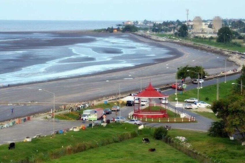A coastal road with a red gazebo, a beach, and a distant cityscape. 1