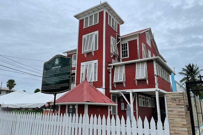 A red brick building with a white picket fence, a red umbrella, and a historical marker. 4
