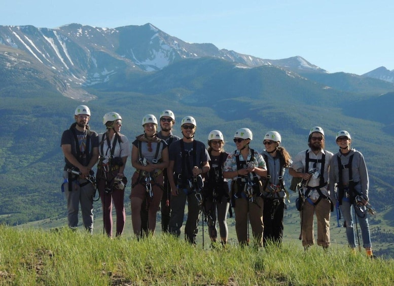 A group of people on a mountain with a clear sky and snow-capped peaks in the background. 3
