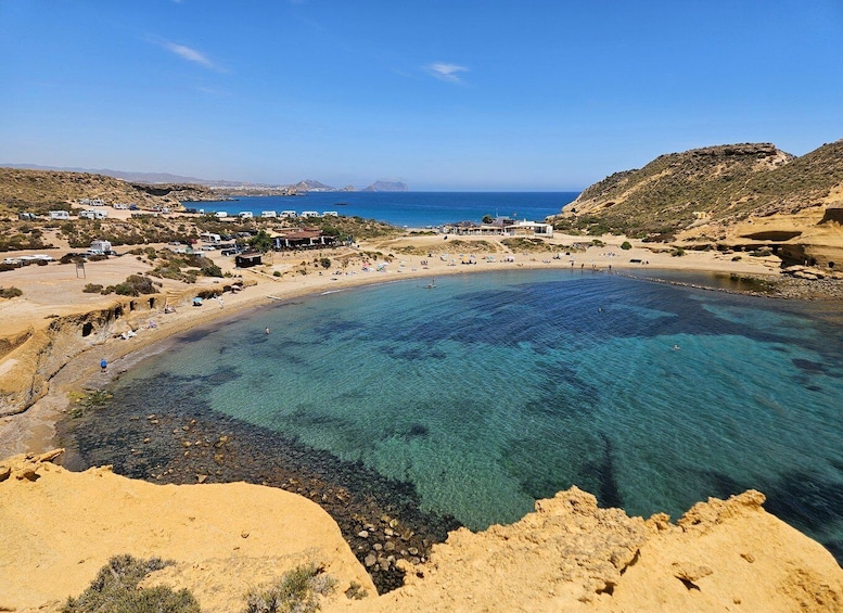 A coastal beach with clear waters, sandy shores, and a few buildings in the background. 1