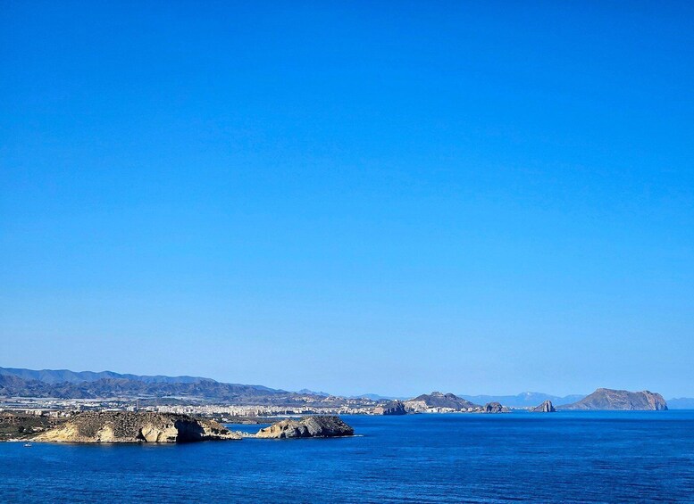 A coastal landscape with clear blue skies, rocky outcrops, and distant mountains. 5