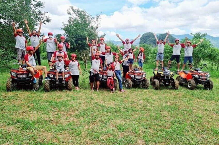A group of people on all-terrain vehicles in a grassy field with trees and hills in the background. 5