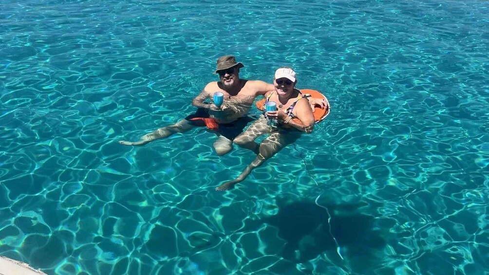 Two people floating in a clear blue pool with a dog. 5