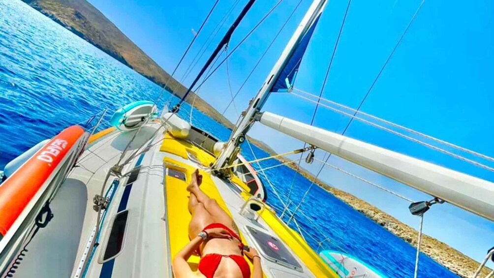 A person lying on a sailboat deck, a lifebuoy, and a clear blue sea with a coastline in the background. 2