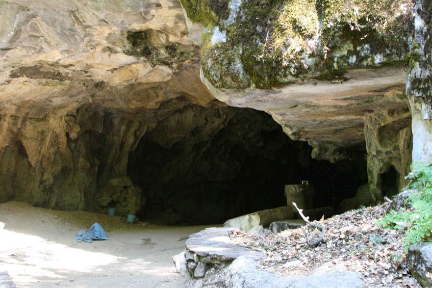 A cave entrance with a moss-covered rock overhang and a small stream flowing into the cave. 4