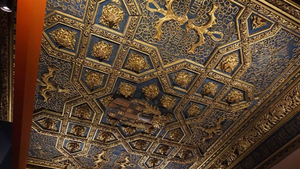 A ceiling with intricate gold and blue geometric patterns and a central relief sculpture. 3