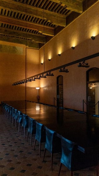 A long table with blue tablecloths and chairs, in a room with wooden beams and wall sconces. 5