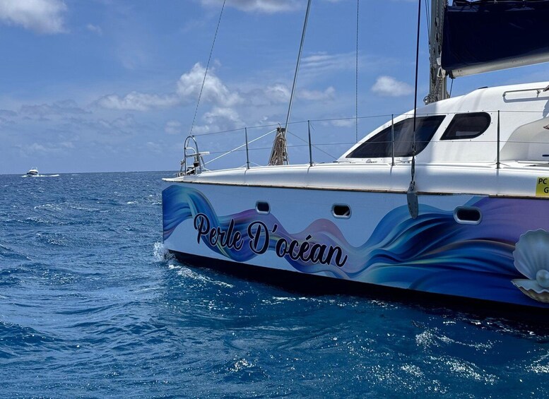 A sailboat named 'Perle D'océan' with a colorful wave design on its side. 3