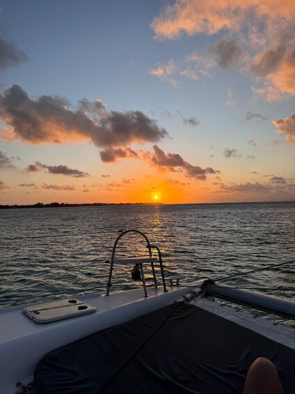 A sunset over a calm sea with a boat's deck and railing in the foreground. 2