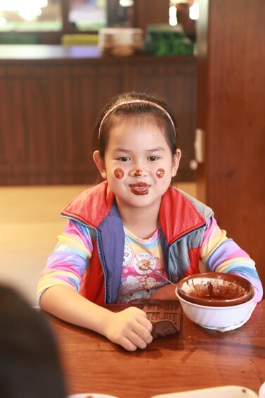 A child sitting at a table with a bowl of chocolate. 4