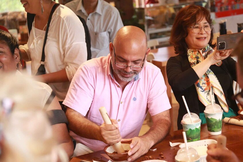 A man grinding something in a bowl at a table with drinks. 1