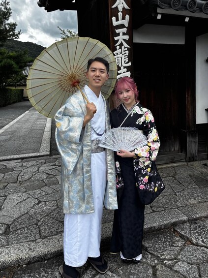 A man and a woman in traditional attire standing in front of a building with a sign. 2