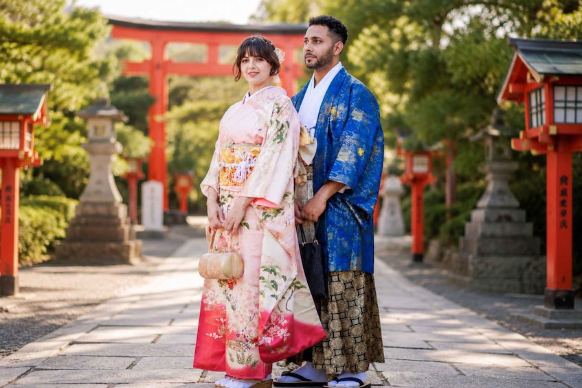 A couple in traditional Japanese attire standing in front of a torii gate. 1