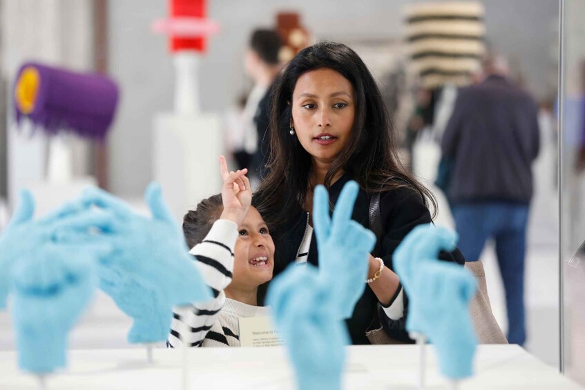 A person in a black jacket and a child in a striped sweater at a table with blue gloves in the foreground. 2
