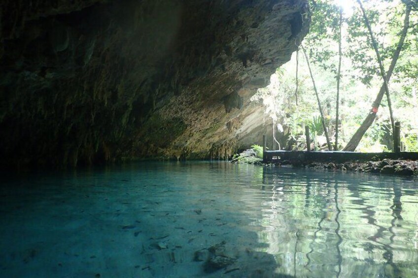 A cave with clear water, a boat, and trees. 5