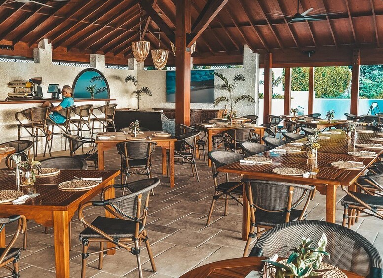 An outdoor restaurant with wooden tables and chairs, a bar area, and a view of the outdoors. 2