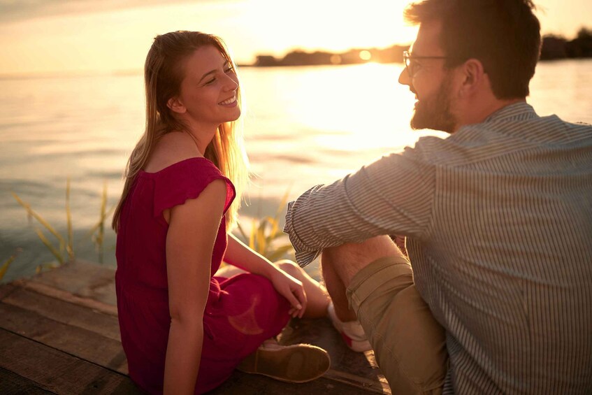 A couple sitting on a wooden dock by a body of water during sunset. 1