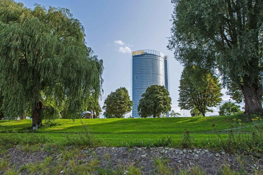 A park with a weeping willow tree, a grassy hill, and a modern glass building in the background. 3