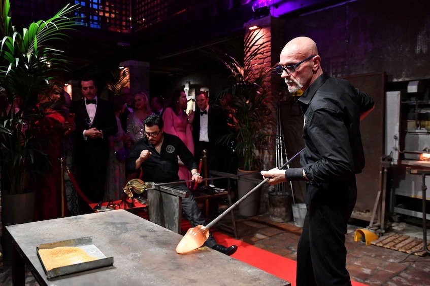 A person holding a long metal rod, possibly a tool, in a dimly lit indoor setting with red carpet and potted plants. 4