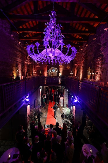 An ornate chandelier in a dimly lit venue with brick walls and a red carpet. 3