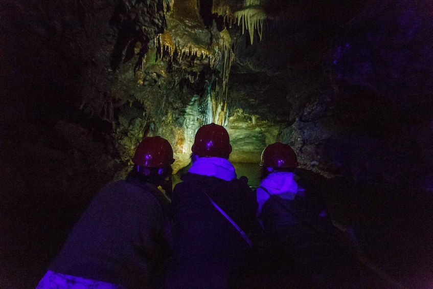 Three people in helmets observing cave formations. 5