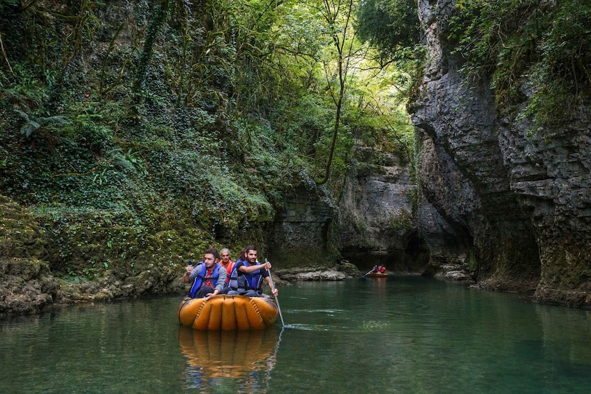 A group of people on an inflatable raft in a river surrounded by dense forest and rocky cliffs. 3