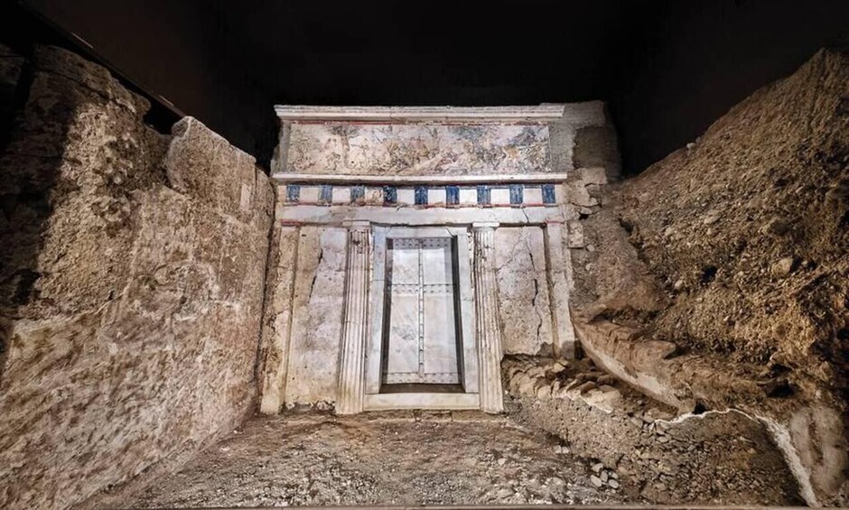 An ancient tomb with a central door, flanked by stone walls, and a tiled frieze above the door. 4
