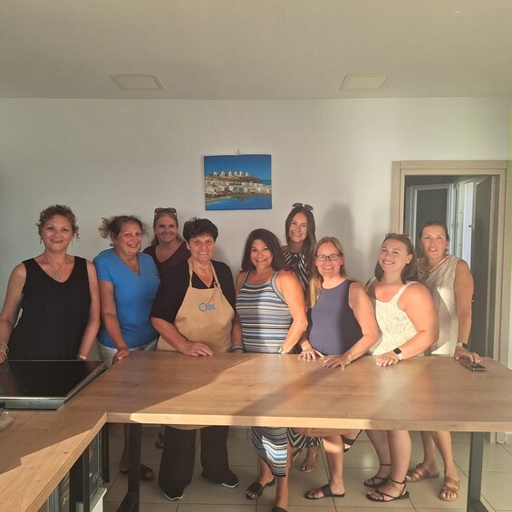 A group of people standing in a kitchen with a painting of a coastal scene on the wall. 2