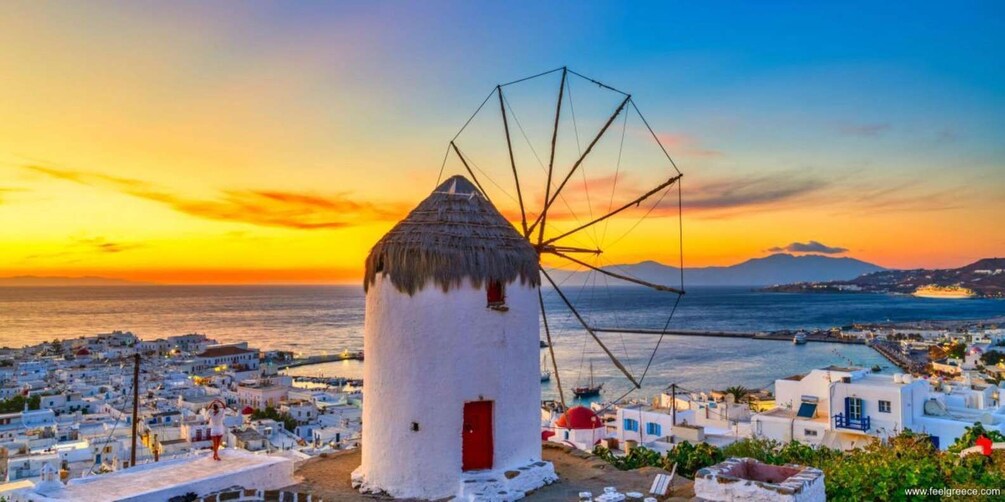 A white windmill with a red door, surrounded by white buildings, at sunset. 3