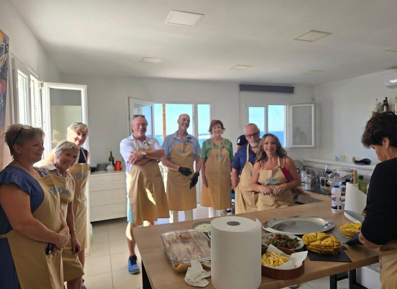 A group of people in a kitchen with aprons, a roll of paper towels, and food items on the counter. 5