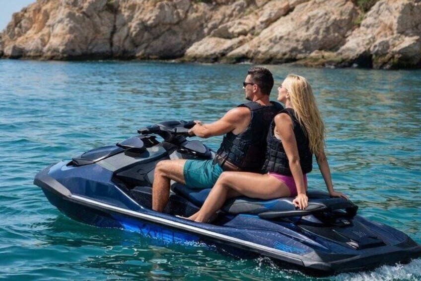 A couple on a jet ski in a body of water with rocky terrain in the background. 4