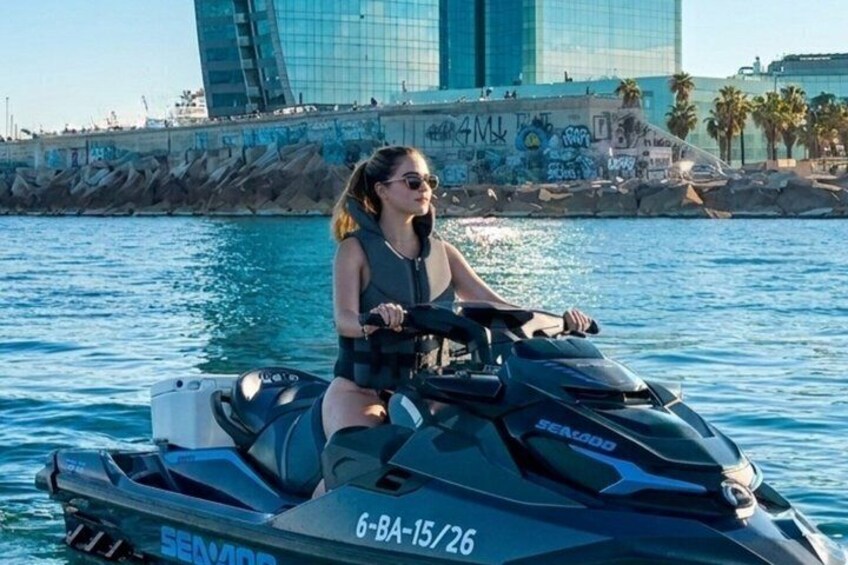 A person riding a jet ski on water with a cityscape in the background. 1