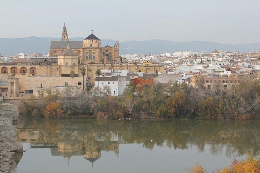 A historic cityscape with a prominent cathedral, a calm river reflecting the buildings, and a backdrop of mountains. 2