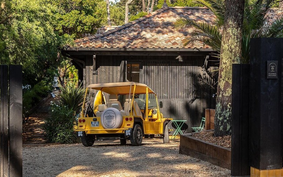 A yellow off-road vehicle parked in front of a rustic building with a tiled roof, surrounded by lush greenery. 3