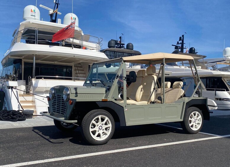 A beige off-road vehicle parked in a marina with yachts in the background. 2