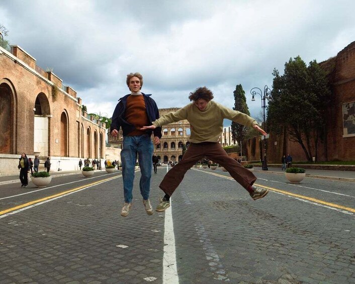 Two people jumping in the middle of a cobblestone street with historical buildings in the background. 1