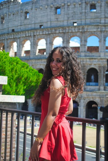 A person in a red dress standing in front of the Colosseum in Rome. 2